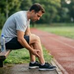 Coureur assis sur un banc extérieur, inspectant sa blessure au mollet avant de reprendre le sport